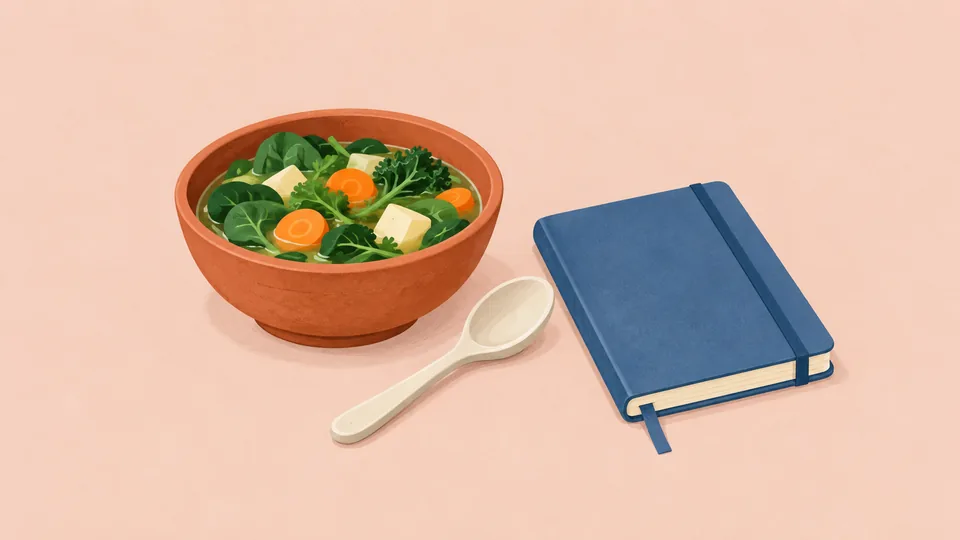 En orange skål med grønne blade, gulerødder og tofu, en hvid ske og en blå notesbog.
