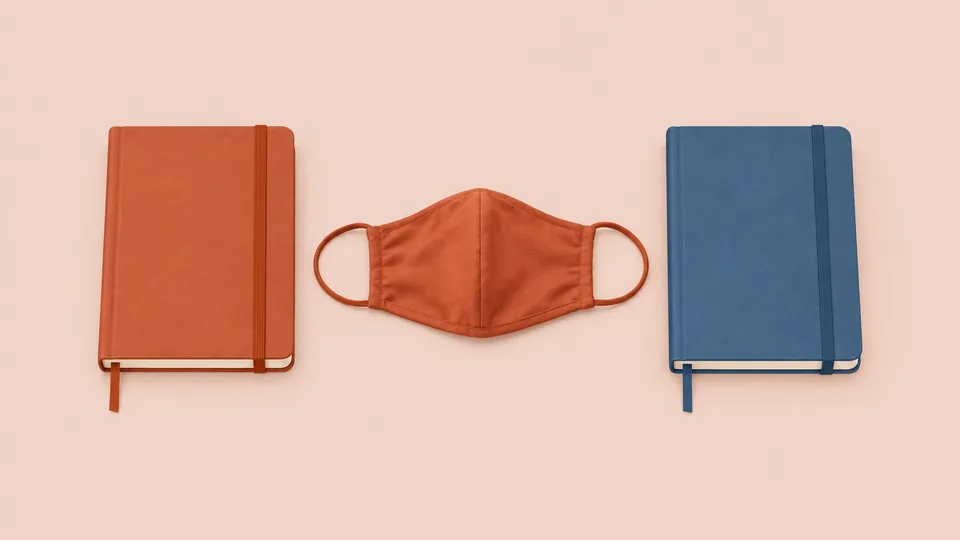 En orange maske og to notebooks i orange og blå på lyserød baggrund.